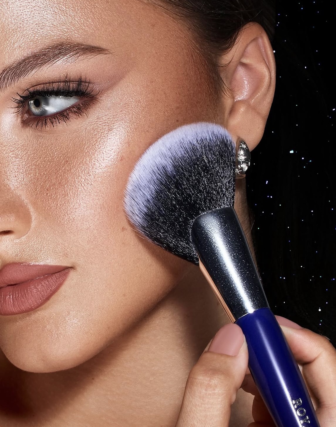 A close-up of bronze cheek highlight, softly smoked liner and a fluffy makeup brush.