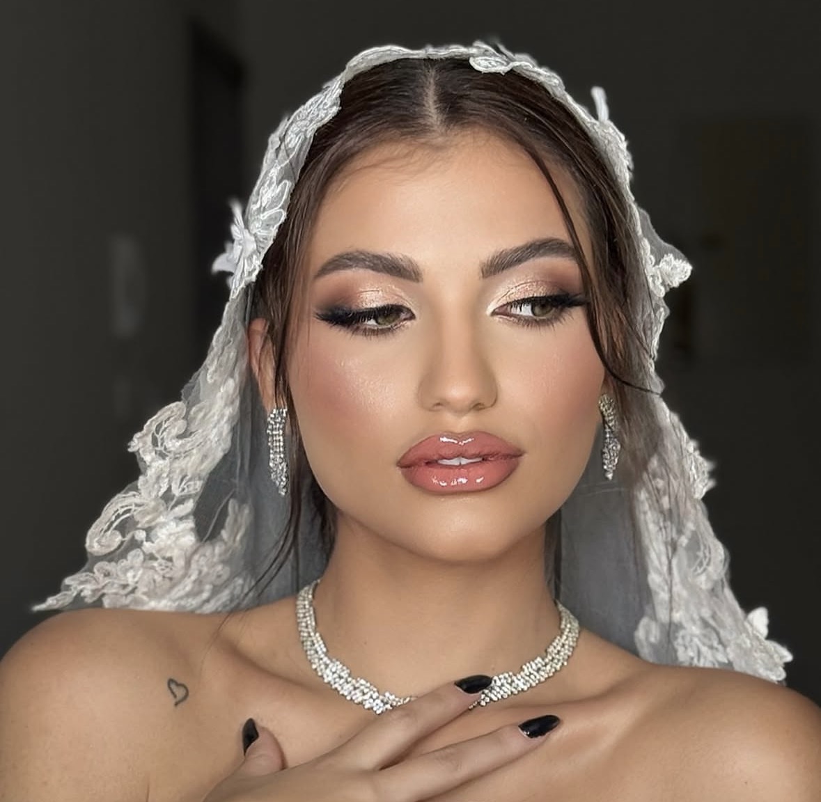 Bridal makeup with champagne eyeshadow, sculpted brows and glossy nude lips beneath a lace veil.