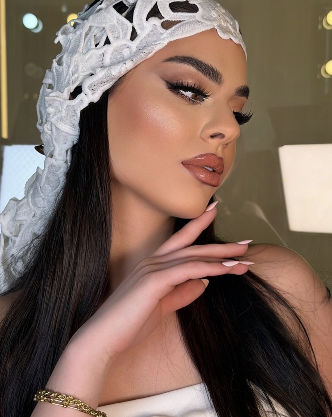 Warm bronze bridal makeup, winged liner and a glossy rose lip with a lace headpiece.