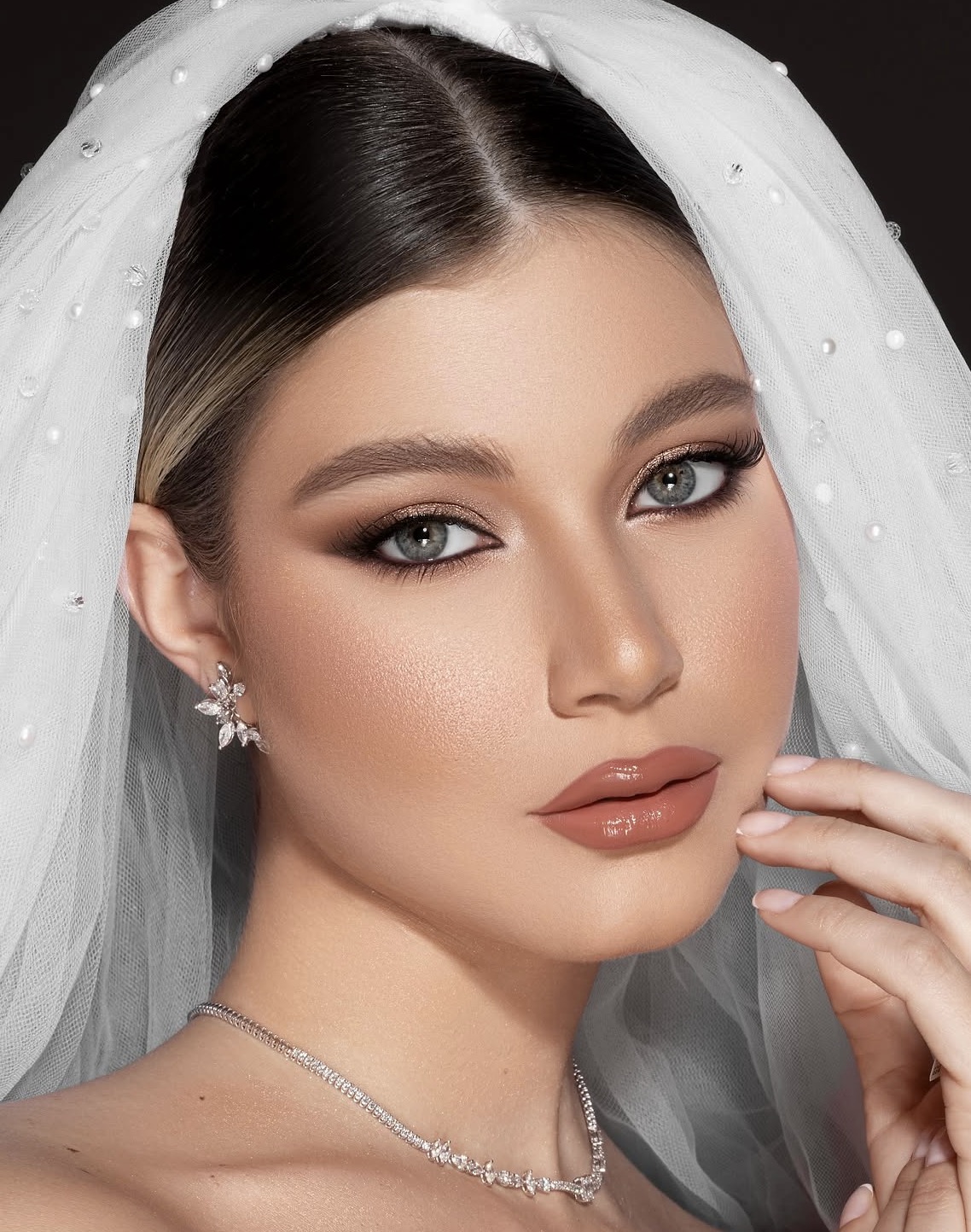 Bridal makeup with softly defined eyes, glowing skin and a warm rose lip, framed by a pearl-dotted veil.